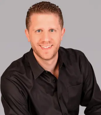 Smiling man in a black shirt against a gray backdrop.