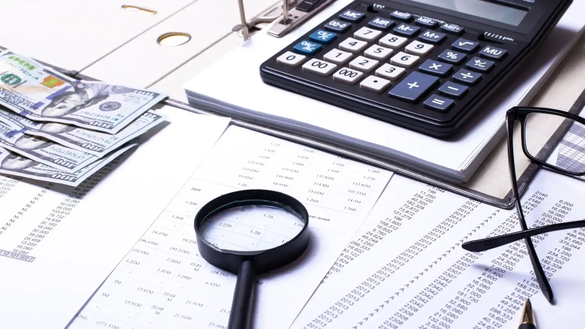 Magnifying glass, calculator, and financial documents on a desk.