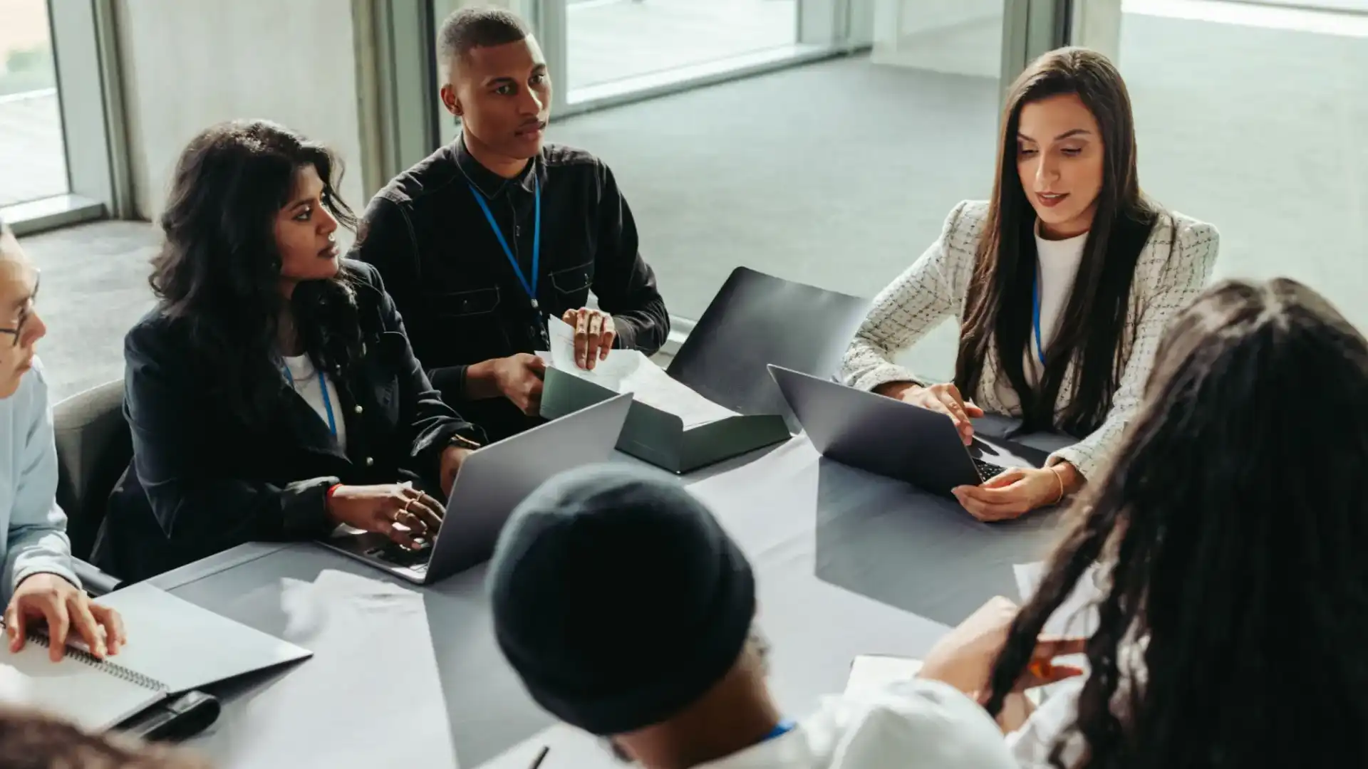 A diverse group discussing work around a table with laptops.