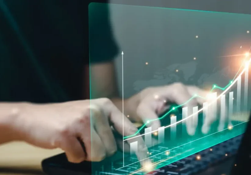 Hands typing on a futuristic transparent laptop with digital financial graphs.