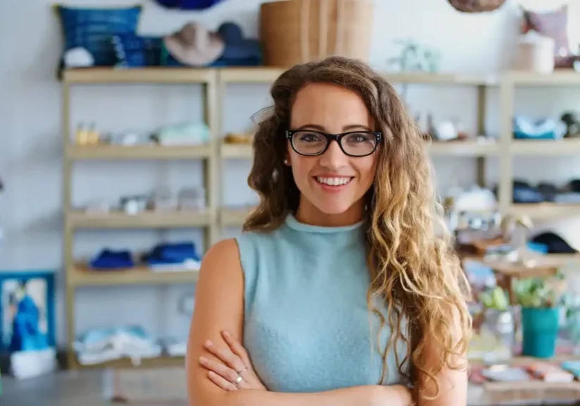 Smiling woman with glasses and curly hair in a cozy, well-lit room.