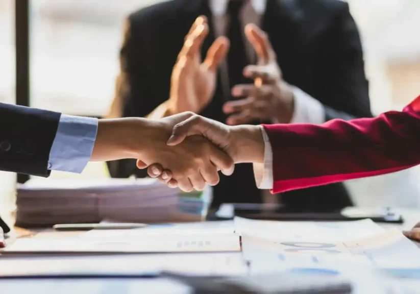 Two people shaking hands over a desk in a professional setting.