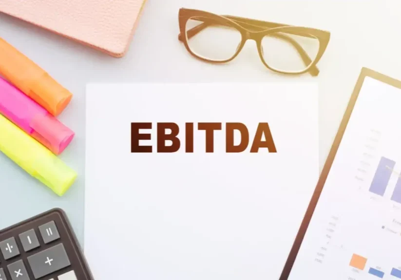 A paper with 'EBITDA' written, surrounded by office supplies.