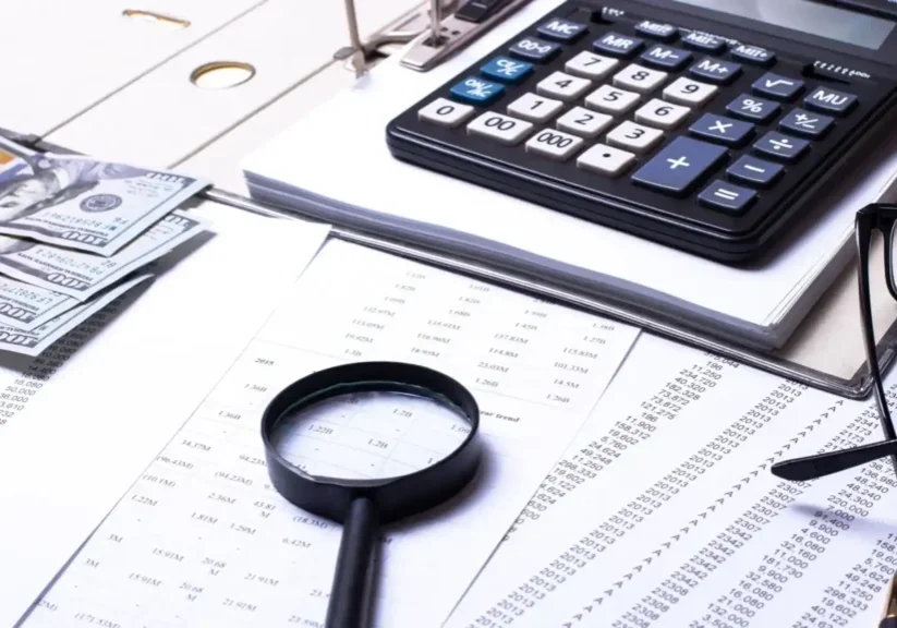 Magnifying glass, calculator, and financial documents on a desk.